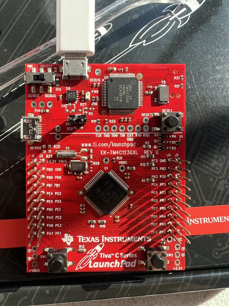 A red Texas Instruments Tiva C Series LaunchPad microcontroller board with a USB cable plugged in.