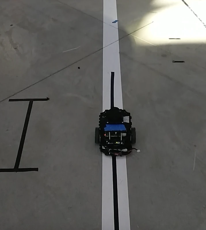 A small wheeled robot on a concrete floor, driving along a dark line laid down the middle of a white stripe.